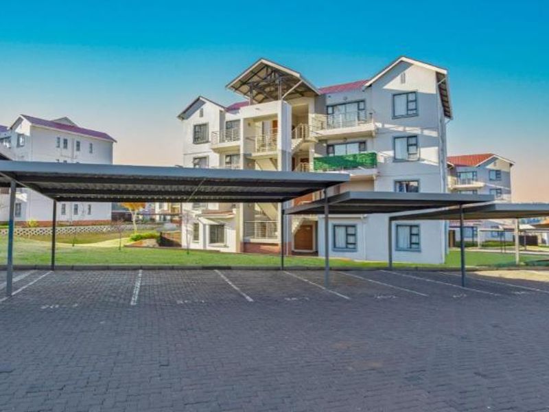 Exterior view of an apartment complex featuring covered parking bays, paved driveway, and multi-story residential units with balconies.