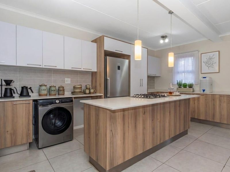 Modern kitchen featuring wood-grain and white cabinetry, stone countertops, a central island with a gas hob, and tiled flooring.