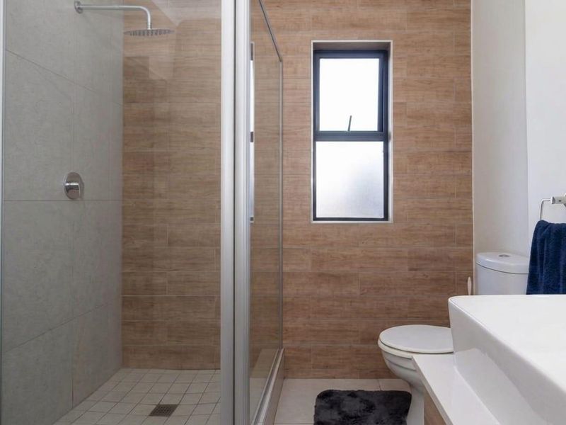 Modern bathroom featuring a walk-in shower with glass enclosure, rain shower head, vanity basin, and contemporary wood-look wall tiling.