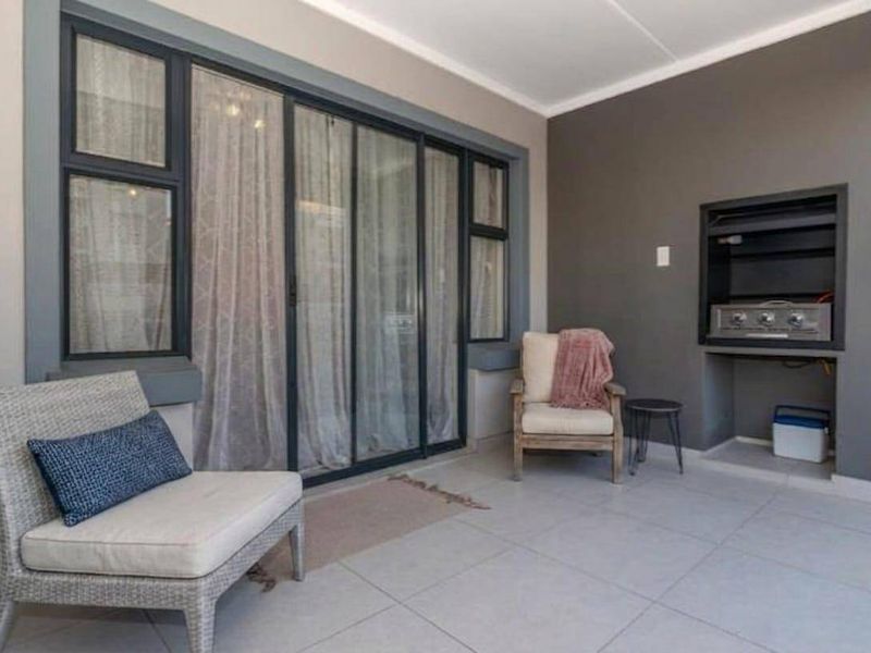 Covered patio area featuring tiled flooring, a built-in braai, and large sliding glass doors providing access to the interior.