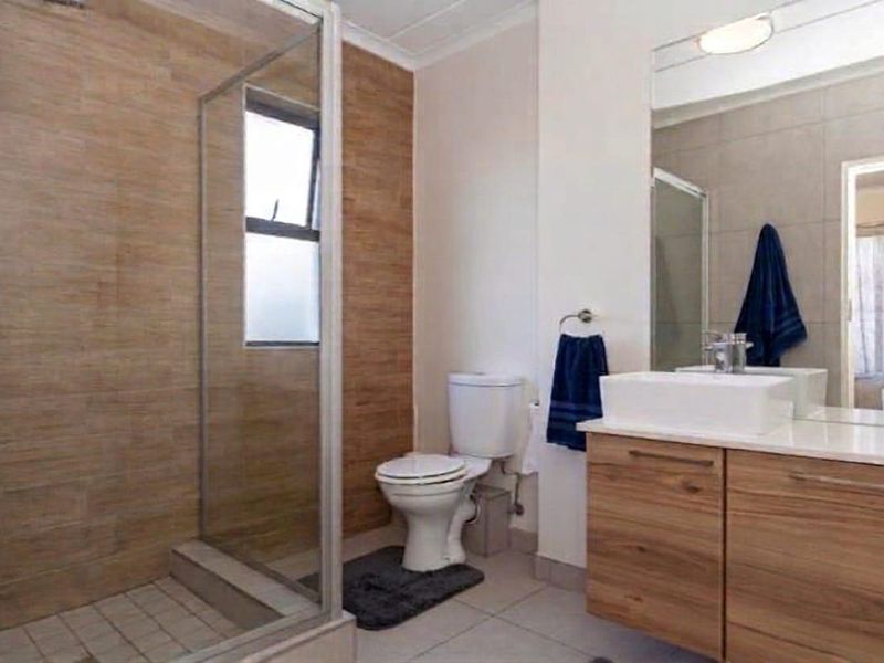 Modern bathroom featuring a glass-enclosed shower with wood-look tiling, a contemporary vanity with a vessel sink, and a large wall mirror.