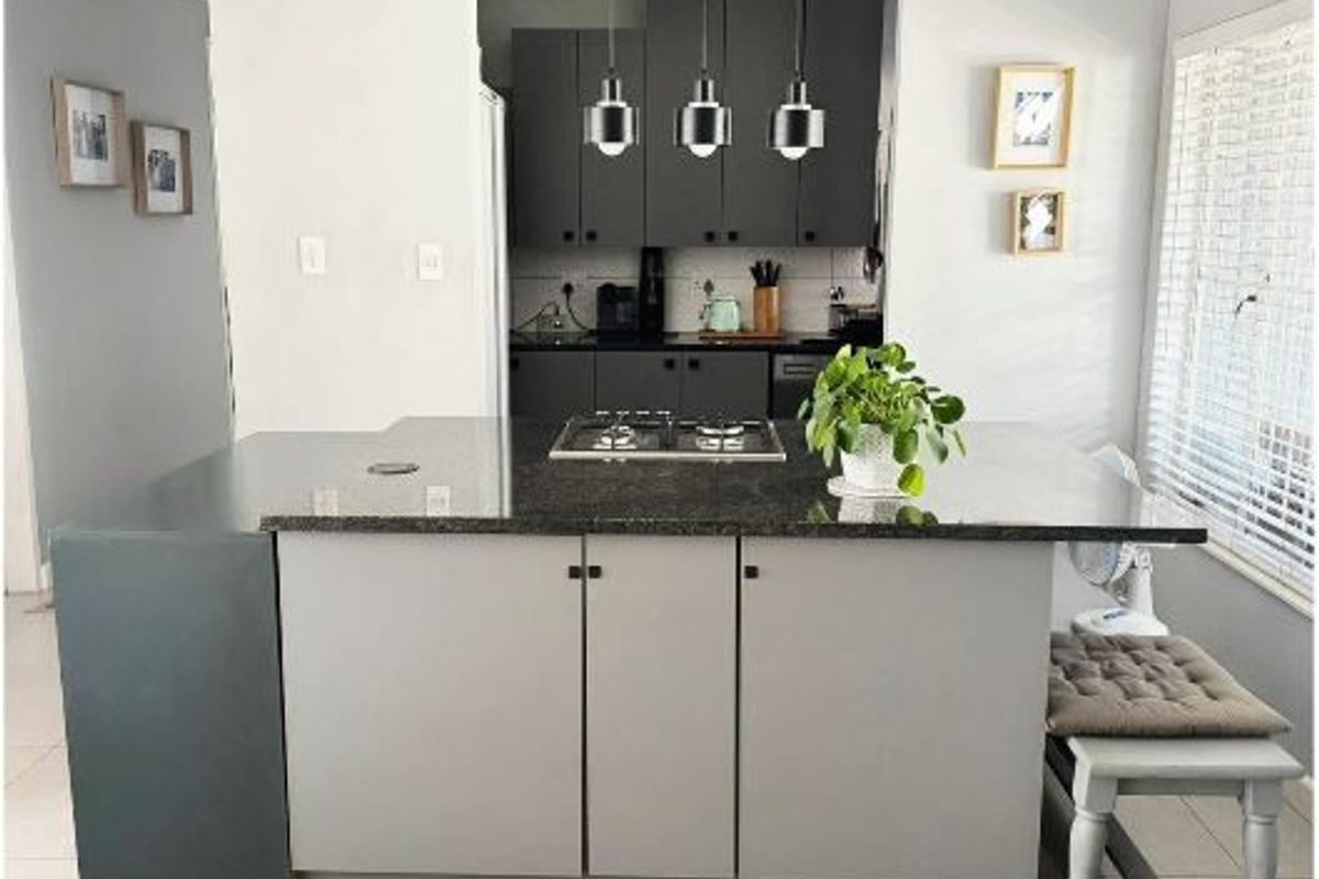 Modern kitchen featuring a central island with a granite countertop, integrated gas hob, and contemporary dark cabinetry with stylish pendant lighting.
