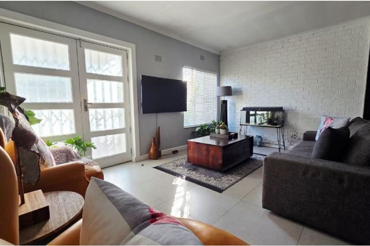 A bright living room featuring large french doors, tiled flooring, and a white painted exposed brick feature wall.