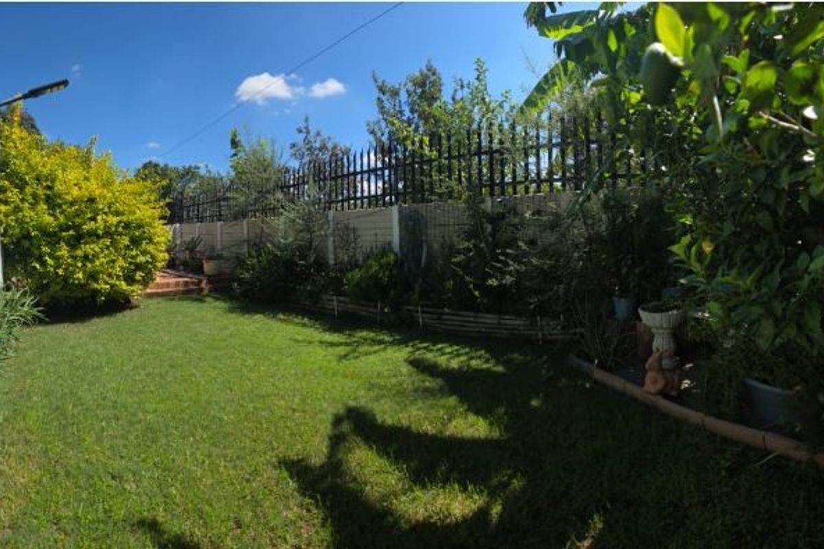 A private rear garden featuring a well-maintained lawn, established greenery, and secure perimeter fencing with a precast concrete wall.