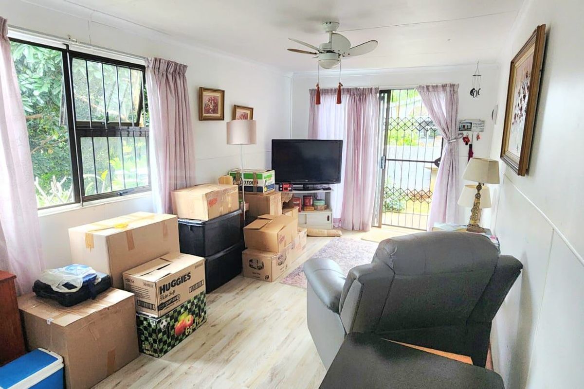 A living room featuring laminate flooring, a ceiling fan, and a sliding glass door with a security gate leading to the exterior.