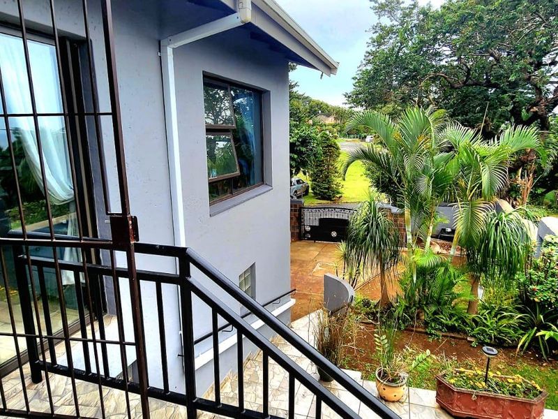 An elevated patio area featuring metal security gates and railings, overlooking a landscaped garden with mature trees and boundary walling.