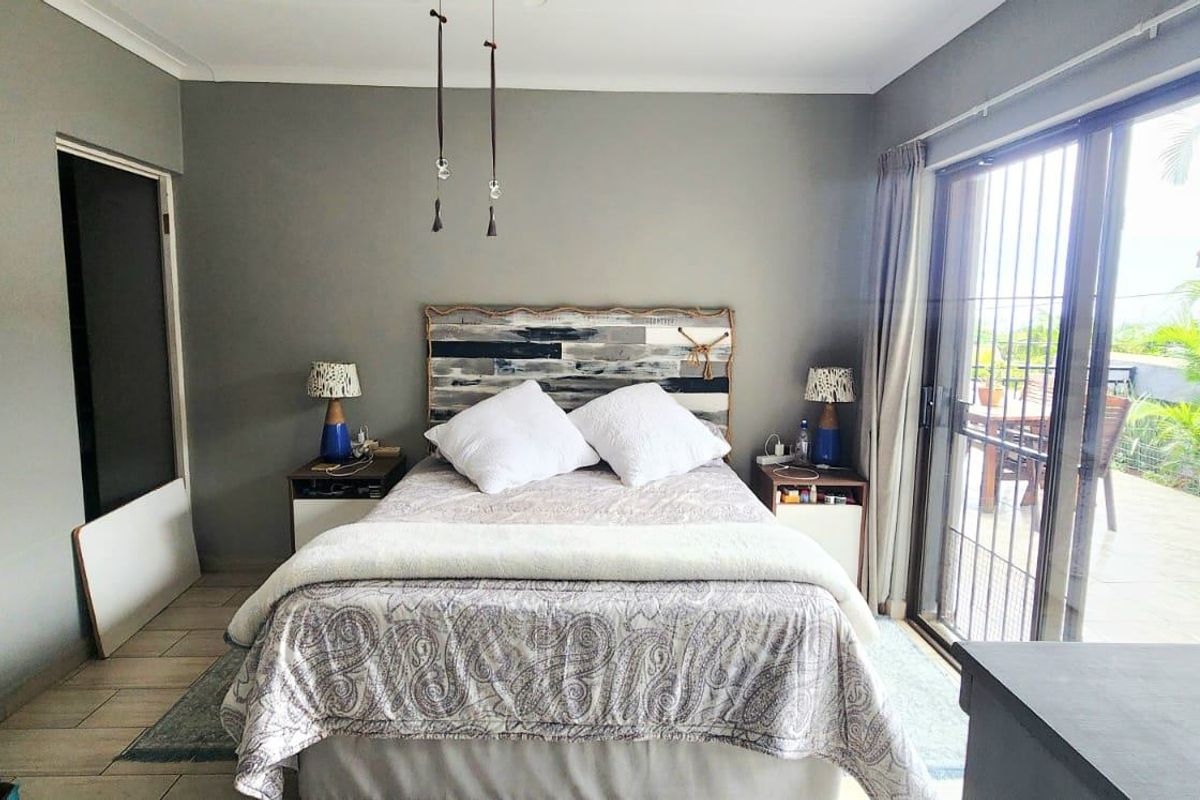 A well-lit bedroom featuring neutral grey walls, tiled flooring, and large sliding glass doors providing direct access to an outdoor patio area.