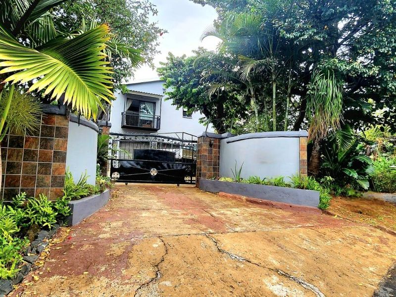 Front entrance view featuring a secure wrought iron gate, masonry boundary walls with decorative tiling, and a private driveway leading to the property.