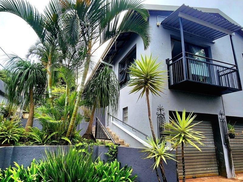 Front elevation of a two-story house featuring a double garage, an upper-level balcony with metal railing, and a landscaped terraced garden.