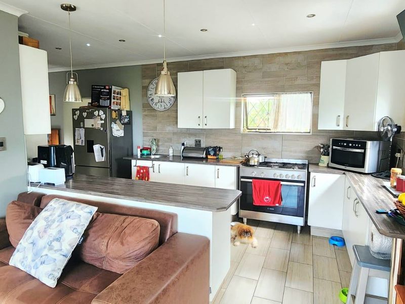 Open-plan kitchen and living area featuring modern white cabinetry, a gas stove, tiled backsplash, and a functional breakfast bar layout.