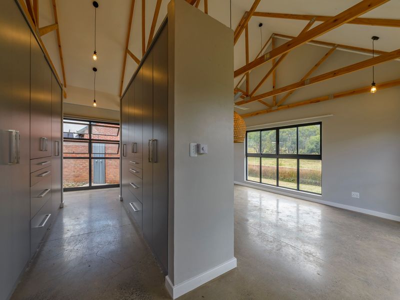 Spacious open-plan area featuring polished concrete floors, exposed timber roof trusses, and extensive built-in cabinetry with large windows providing natural light.