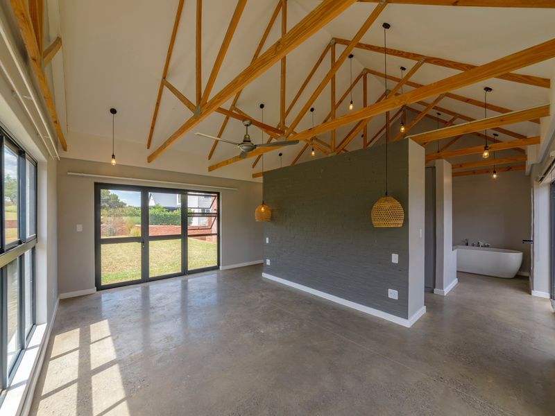 Spacious open-plan living area featuring exposed timber roof trusses, polished concrete floors, and a modern integrated bathroom space with a freestanding tub.