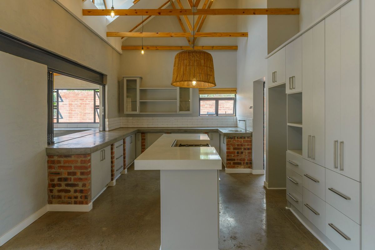 Modern kitchen featuring exposed timber trusses, polished concrete floors, concrete countertops, and custom cabinetry with an integrated island and brick detailing.