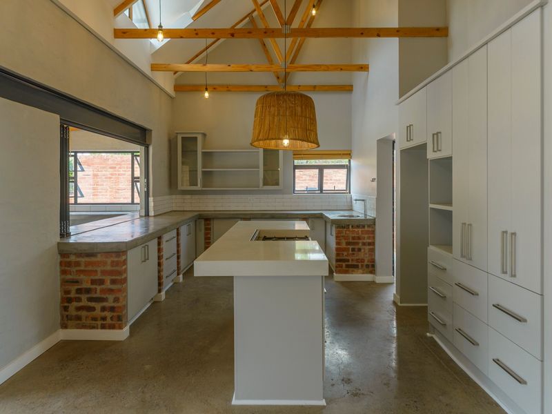 Modern kitchen featuring exposed timber trusses, polished concrete floors, concrete countertops, and custom cabinetry with an integrated island and brick detailing.