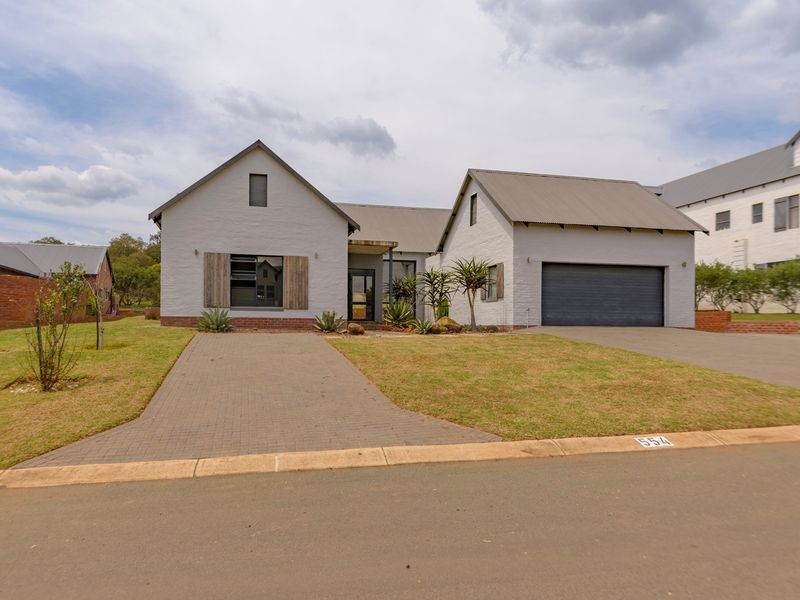 A well-maintained modern single-story house featuring a painted brick facade, pitched metal roof, integrated garage, and a paved driveway.