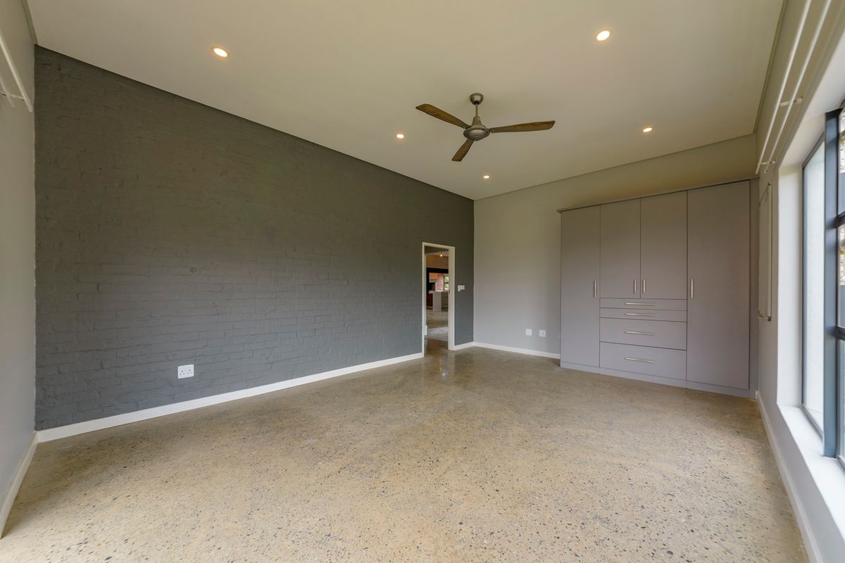 Spacious bedroom featuring polished concrete floors, an exposed brick feature wall, built-in cabinetry, and modern recessed lighting.