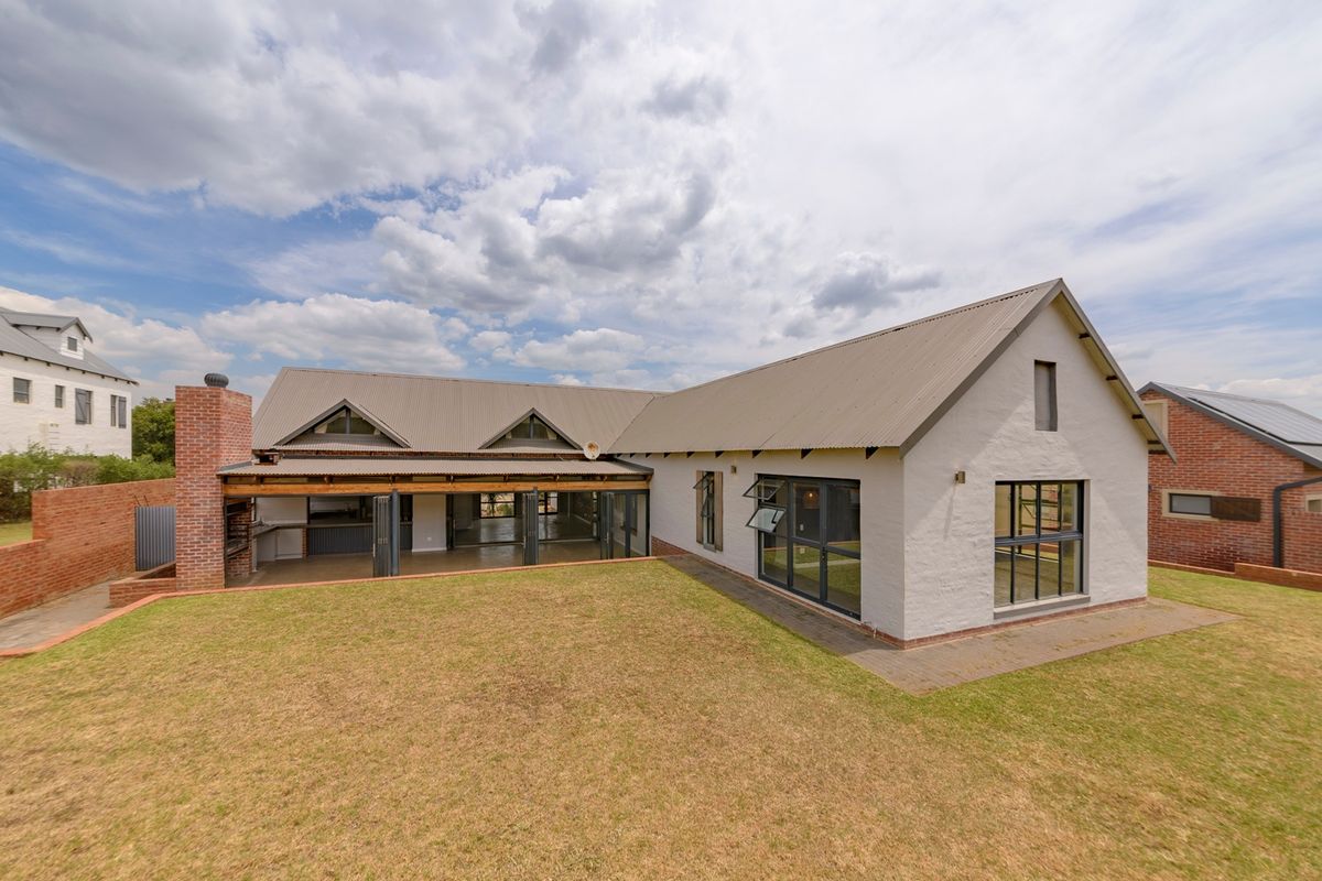 Rear view of a modern farmhouse-style home featuring a covered patio, brick chimney, and expansive lawn area.