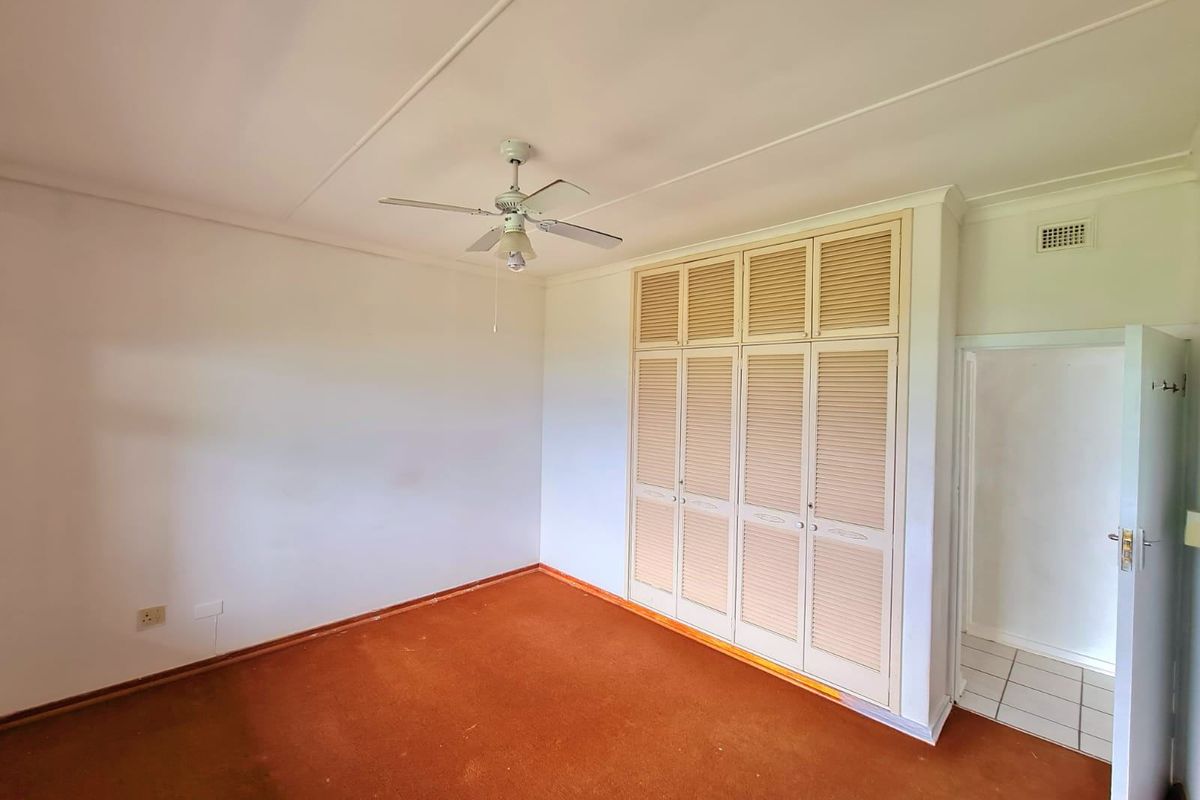 An empty bedroom featuring built-in louvered cupboards, a ceiling fan, and carpeted flooring, offering a blank canvas for renovation.