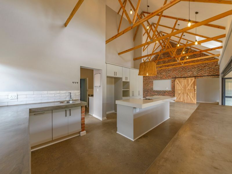 Spacious open-plan kitchen featuring exposed timber trusses, brick feature wall, polished concrete floors, and modern cabinetry with a central island.