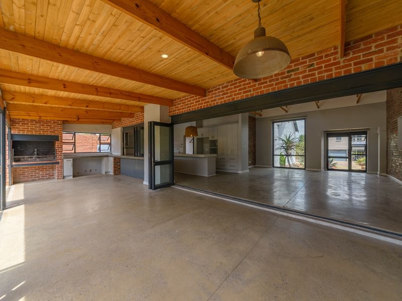 Spacious open-plan living area featuring polished concrete floors, exposed brickwork, timber beam ceilings, and seamless indoor-outdoor flow through large bi-fold doors.