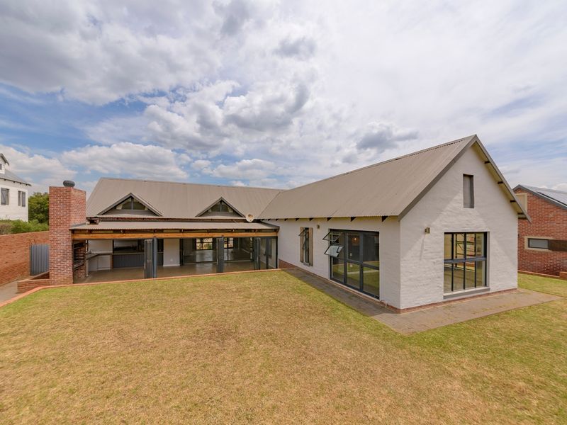 Rear view of a modern farmhouse-style home featuring a covered patio, brick chimney, and expansive lawn area.