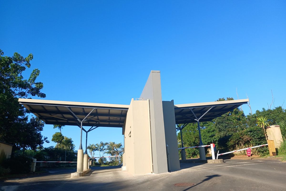 A modern security gatehouse entrance featuring a dual boom gate system and a covered driveway structure, providing controlled access to the residential estate.