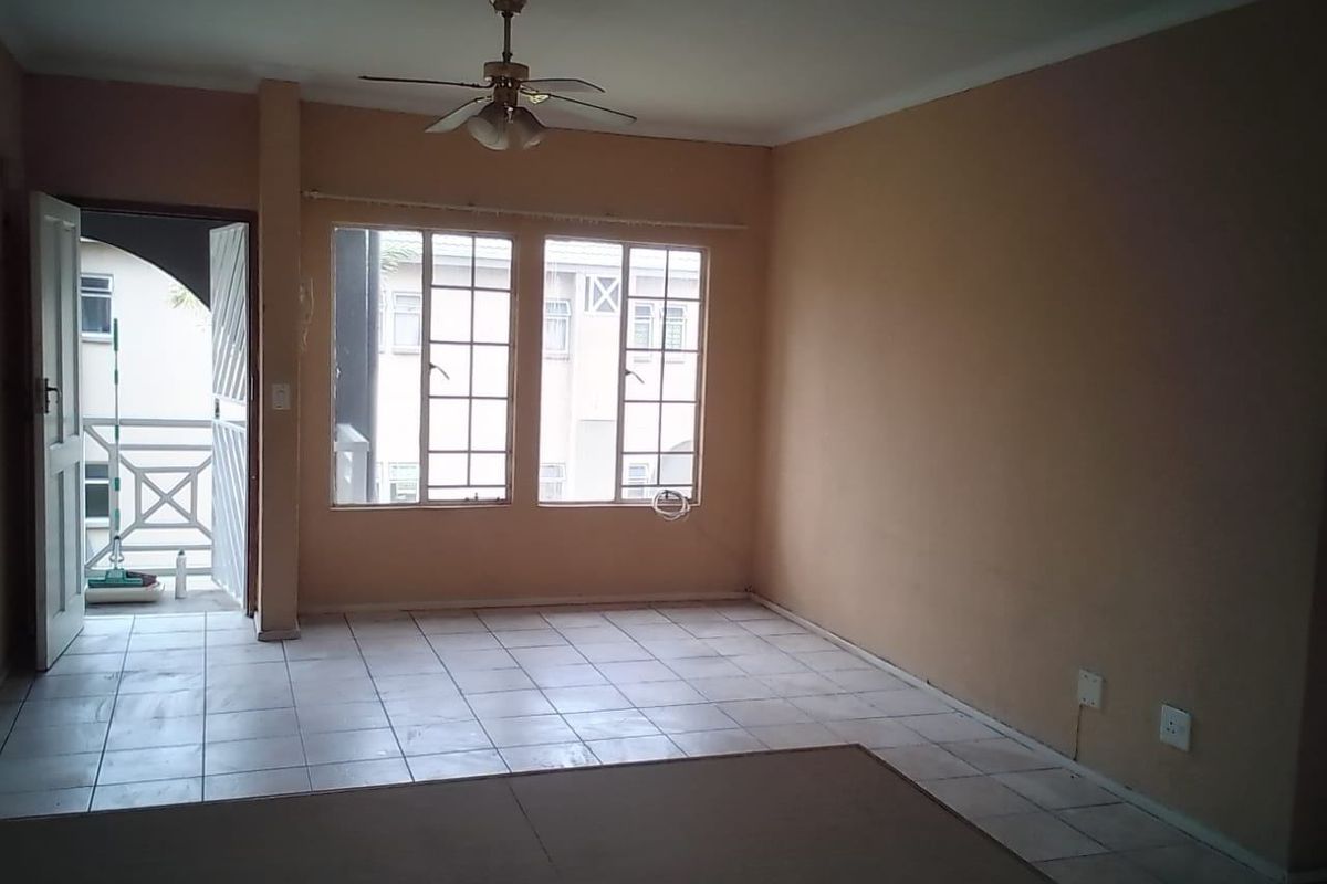 An empty living room featuring tiled flooring, a ceiling fan, and access to an outdoor balcony area through a security gate.