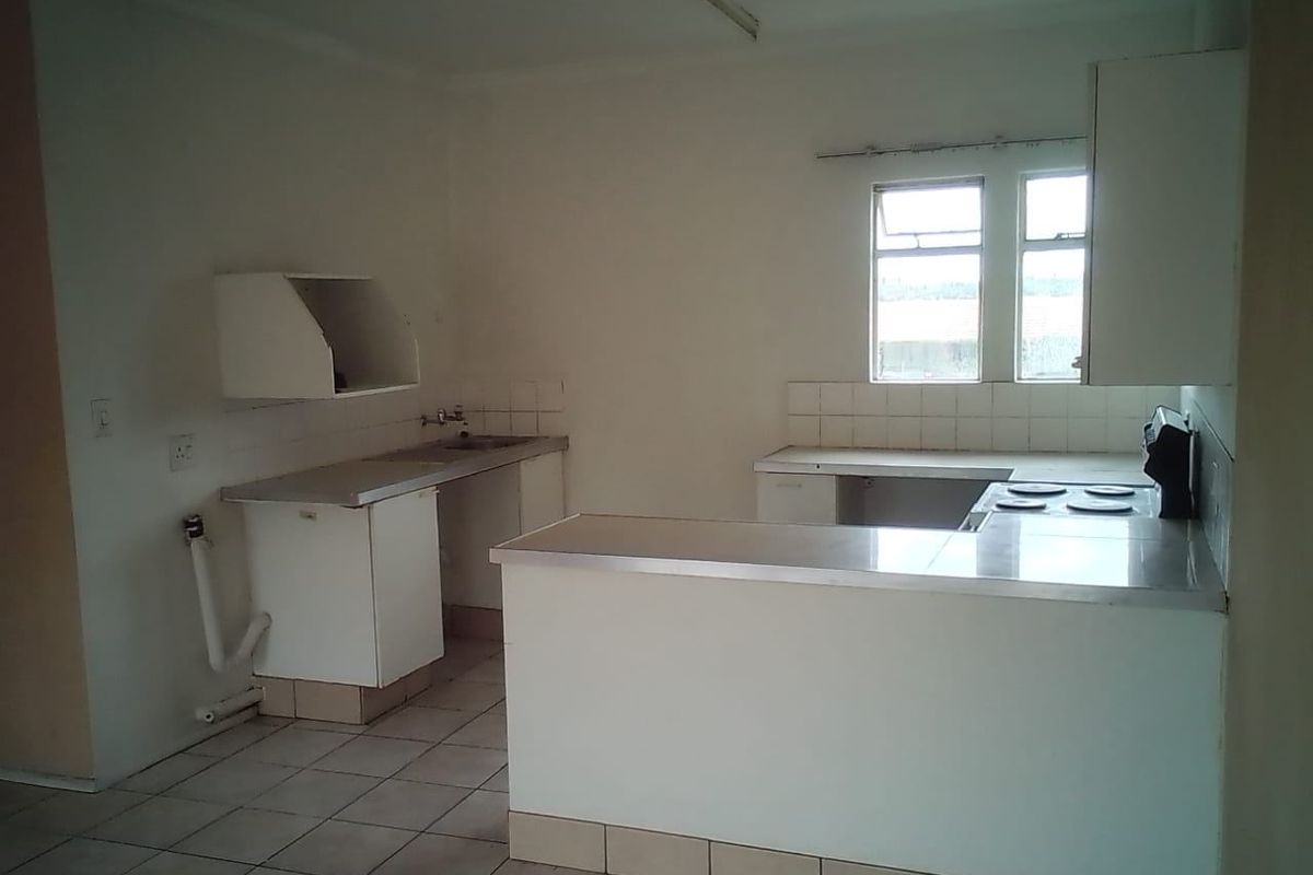 An empty, dated kitchen featuring built-in cabinetry, a stainless steel sink, and an electric hob, offering a blank canvas for renovation.