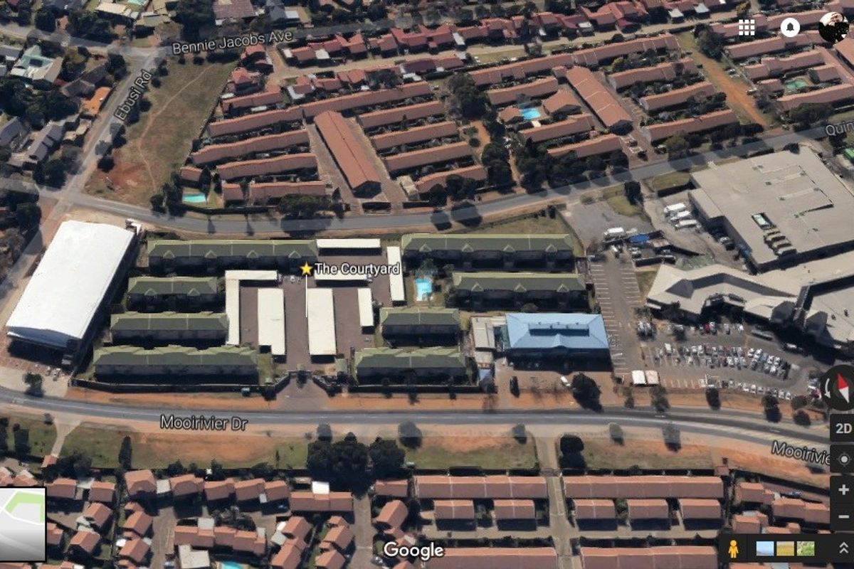 An aerial view of The Courtyard apartment complex showing the layout, parking facilities, and communal swimming pool area.