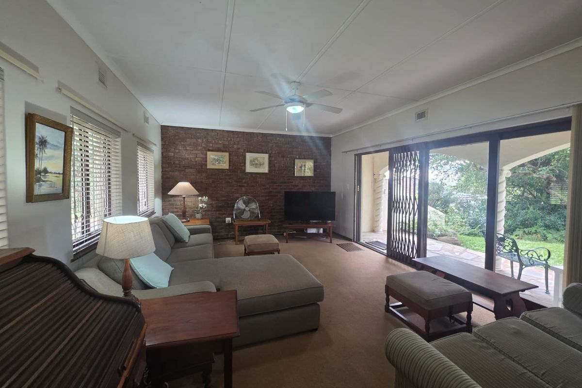 Spacious living room featuring an exposed brick accent wall, ceiling fan, and large sliding glass doors providing direct access to the outdoor patio area.