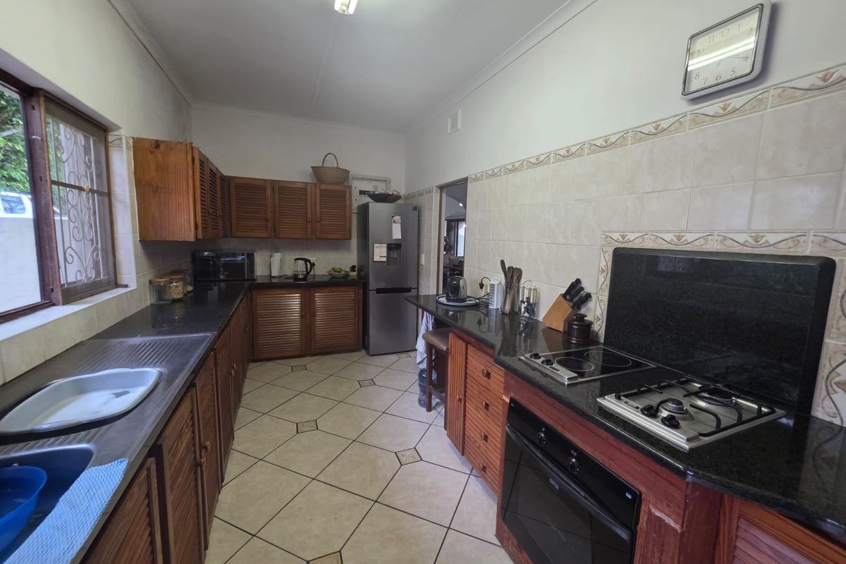A functional kitchen featuring wooden cabinetry, granite countertops, a dual gas and electric hob, built-in oven, and tiled flooring with a backsplash.
