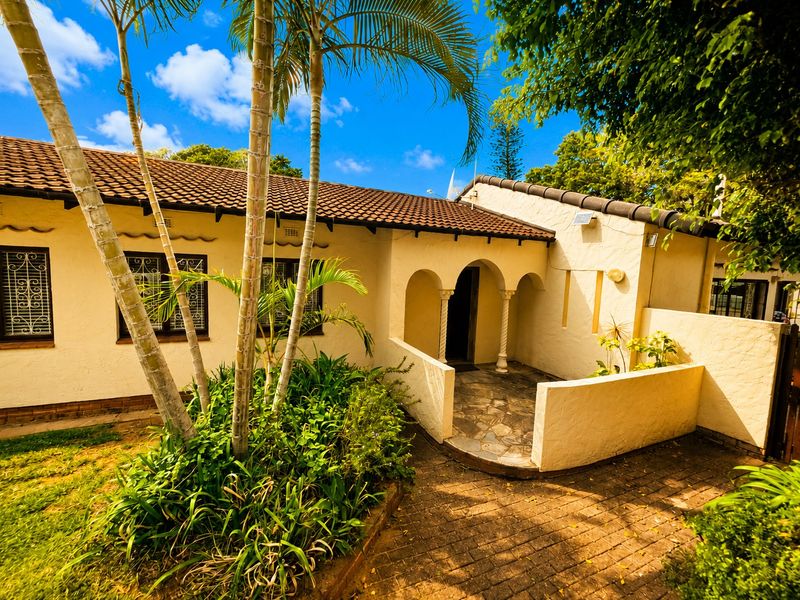 Front elevation of a house featuring a tiled roof, arched entrance, stone-paved patio area, and security bars on the windows.