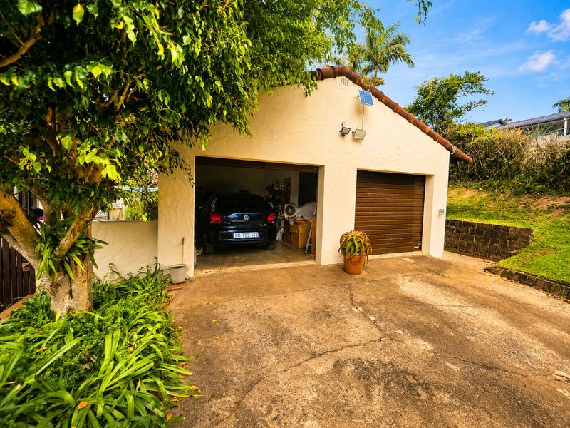 A double garage featuring a roll-up door and concrete driveway, set within a landscaped garden area with a retaining wall.