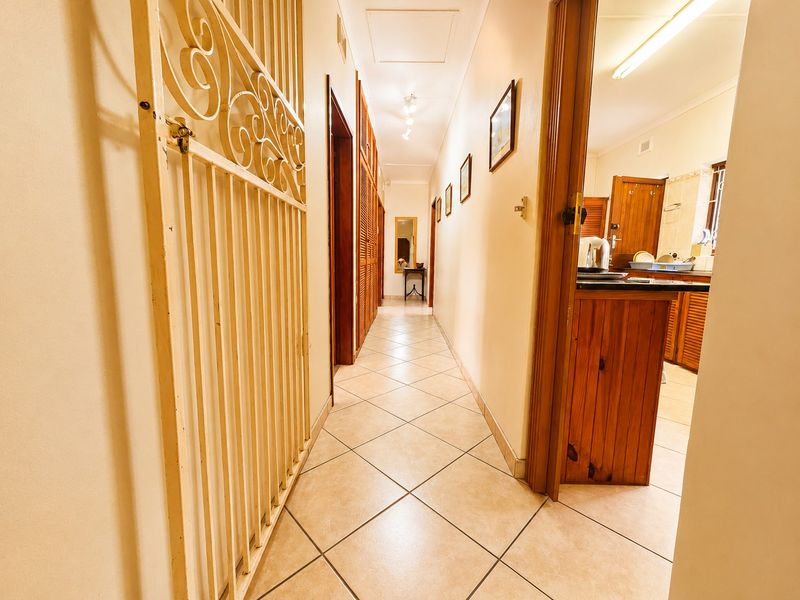 A well-lit hallway featuring tiled flooring, built-in wooden cupboards, and a security gate, providing access to adjacent rooms.