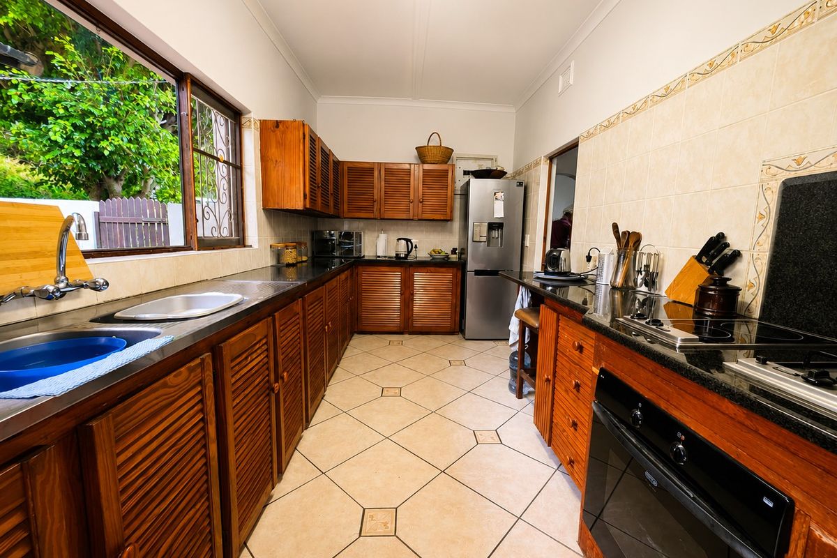 A functional kitchen featuring wooden cabinetry, granite countertops, built-in oven, electric hob, and tiled flooring with a view of the garden.