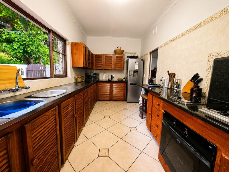 A functional kitchen featuring wooden cabinetry, granite countertops, built-in oven, electric hob, and tiled flooring with a view of the garden.