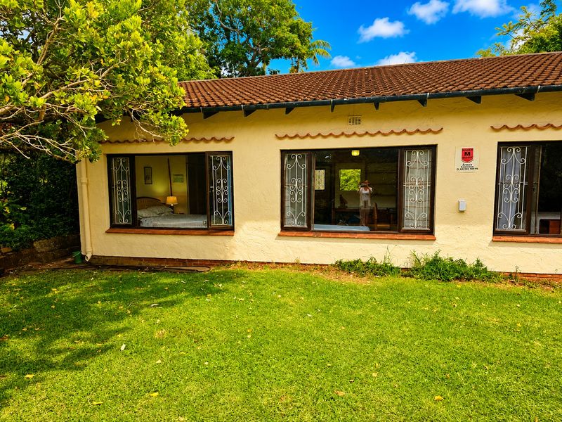 Rear view of the house featuring a lawn, terracotta tiled roof, and security bars on the windows.