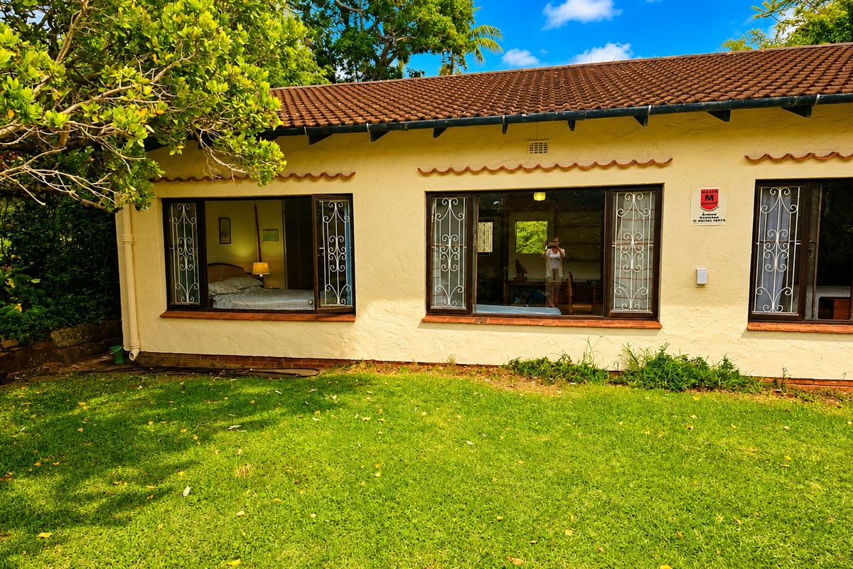 Rear view of the house featuring a lawn, terracotta tiled roof, and security bars on the windows.