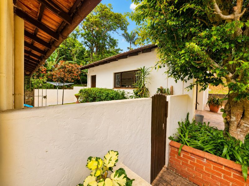 A view of the rear exterior area featuring a paved walkway, brick planter, and a white boundary wall with a timber gate.