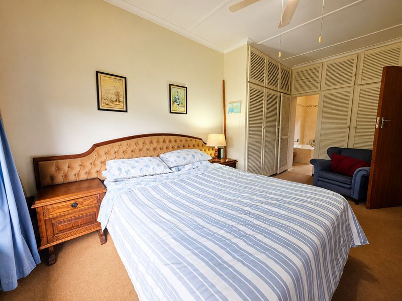 A carpeted bedroom featuring built-in louvered cupboards, a ceiling fan, and direct access to an en-suite bathroom.