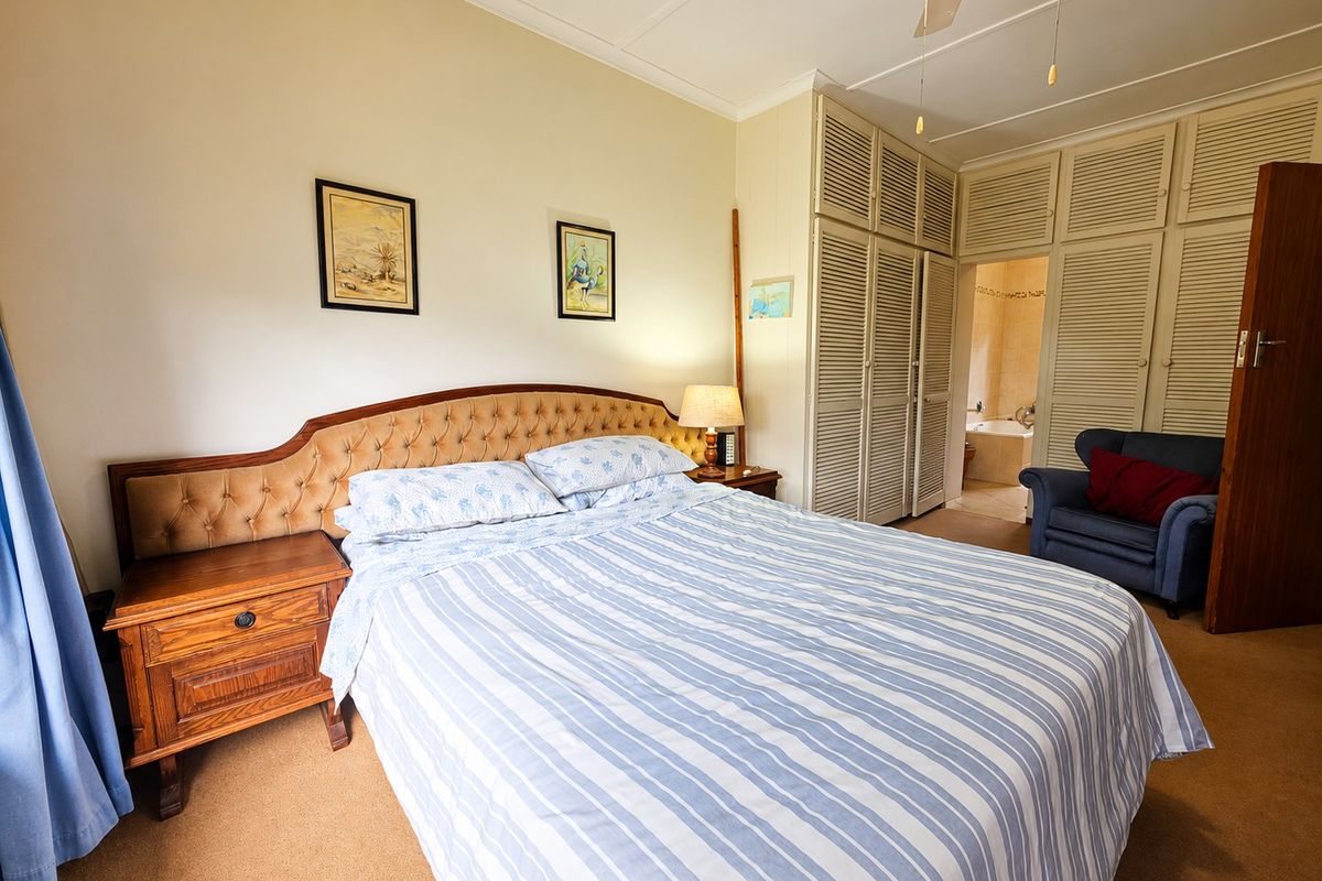 A carpeted bedroom featuring built-in louvered cupboards, a ceiling fan, and direct access to an en-suite bathroom.