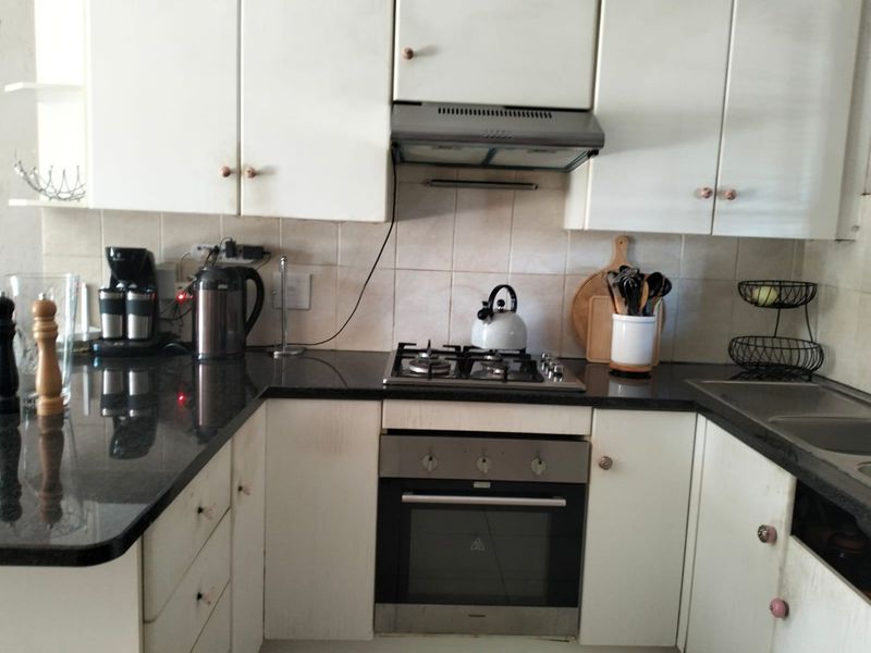 A functional kitchen featuring white cabinetry, dark granite countertops, a built-in gas hob, oven, and extractor fan with a tiled backsplash.