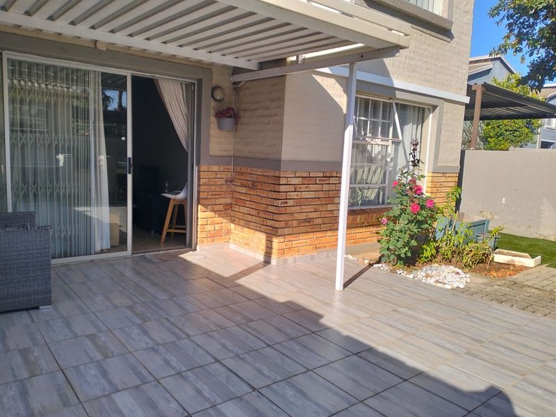 A well-maintained tiled patio area featuring a covered pergola, brick facade detailing, and direct access to the interior through a sliding glass door.