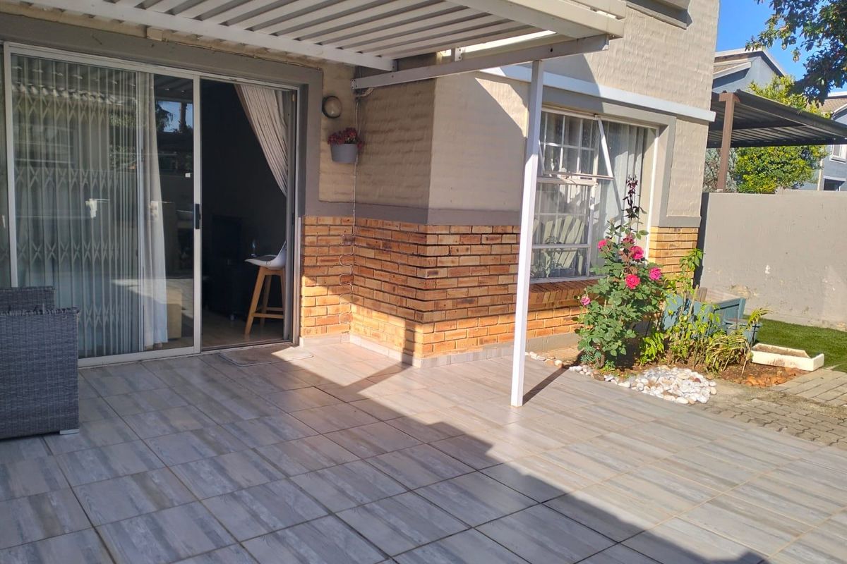 A well-maintained tiled patio area featuring a covered pergola, brick facade detailing, and direct access to the interior through a sliding glass door.