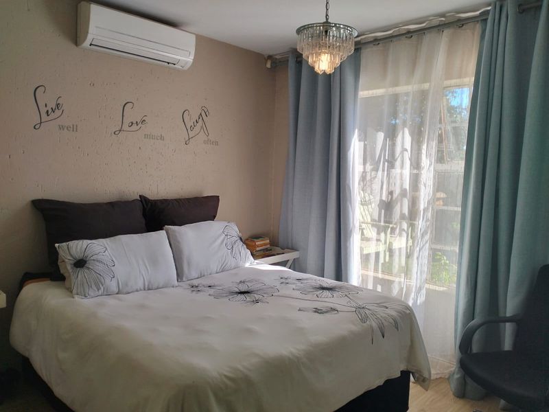 A bedroom featuring a wall-mounted split-system air conditioner, a decorative crystal chandelier, and a sliding glass door providing natural light.