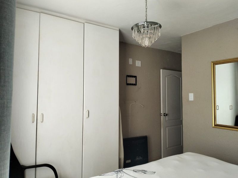 A bedroom featuring built-in white wardrobes, a decorative crystal chandelier, and neutral wall finishes.