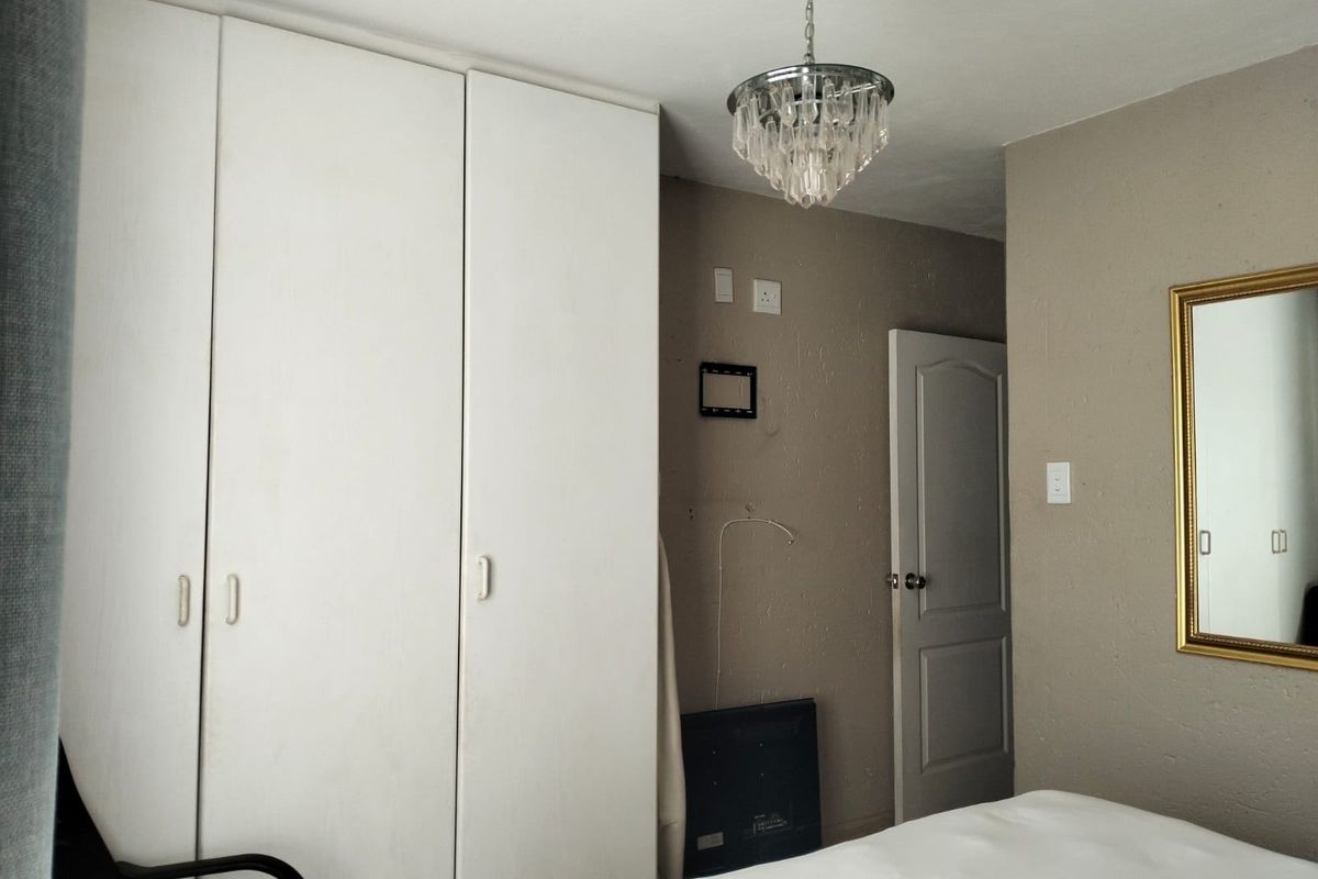 A bedroom featuring built-in white wardrobes, a decorative crystal chandelier, and neutral wall finishes.