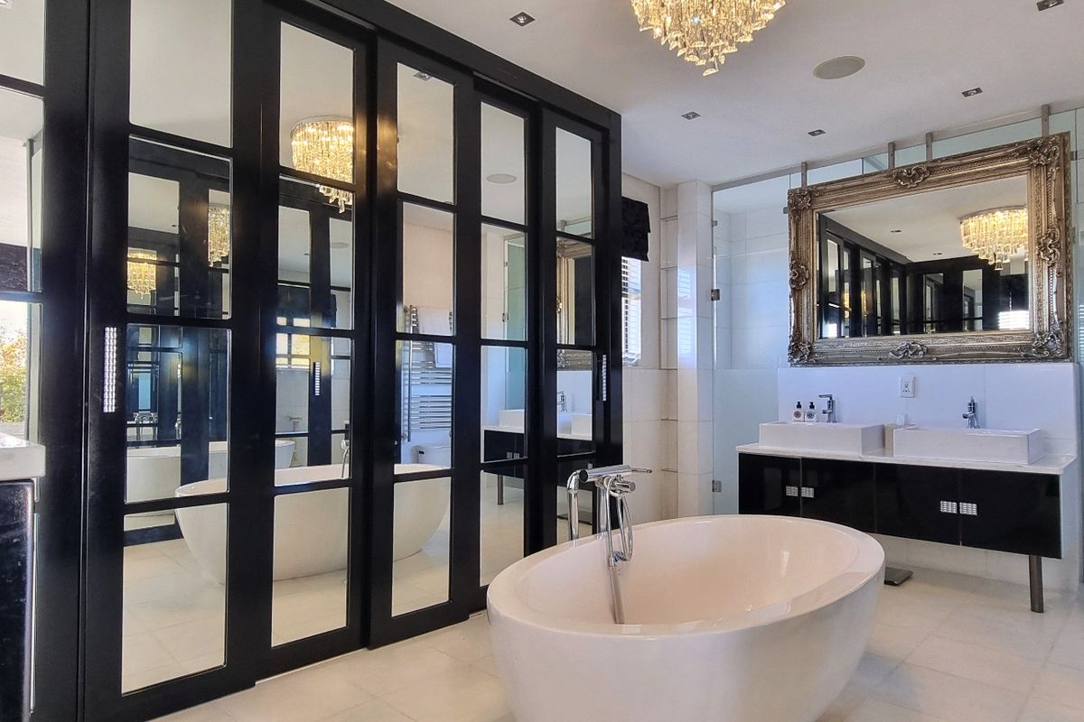 Luxurious modern bathroom featuring a freestanding bathtub, double vanity with integrated mirrors, and elegant black-framed glass partitions.