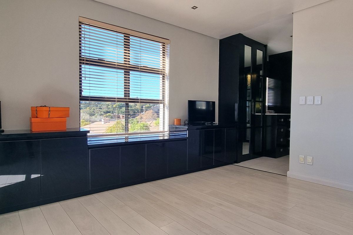 Spacious bedroom featuring modern built-in black cabinetry, light laminate flooring, and large windows with venetian blinds, offering a clean and contemporary aesthetic.