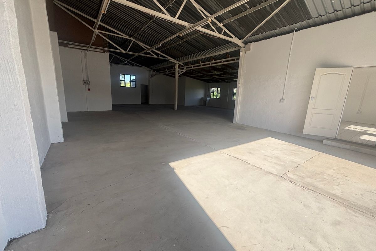 Spacious industrial utility area featuring exposed steel roof trusses, concrete flooring, and white-painted walls, suitable for storage or workshop use.